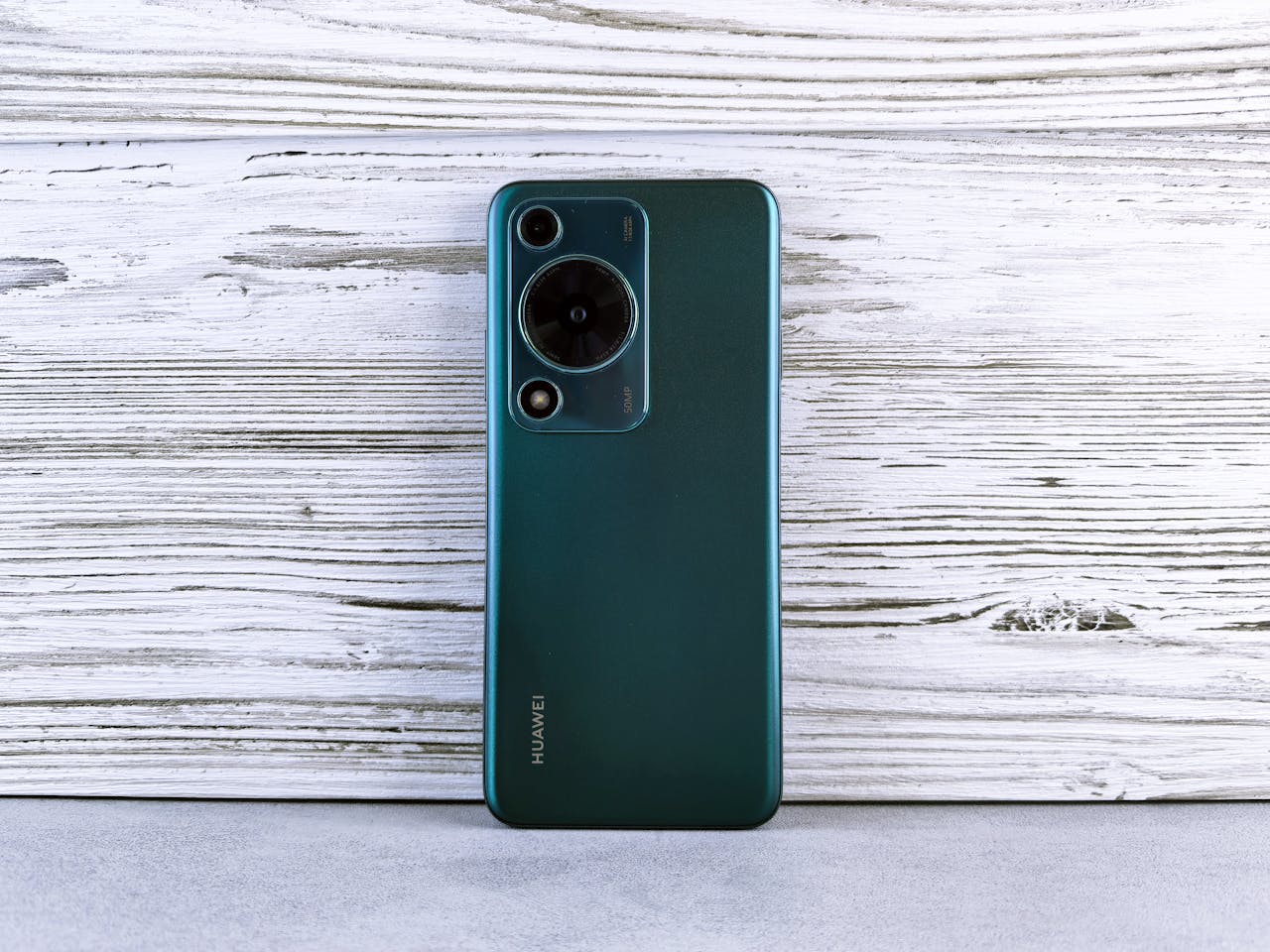 A sleek green smartphone rests on a textured wooden surface, showcasing modern design and technology.